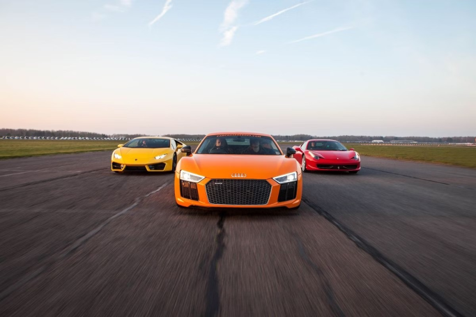 Three sports cars in vibrant orange, yellow, and red are lined up on a racetrack.