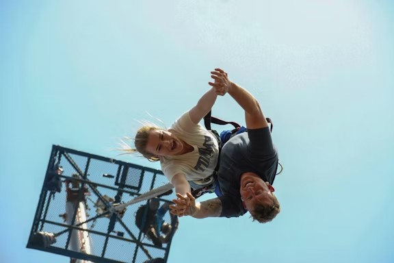 A person bungee jumping, held by an instructor, against a clear sky.