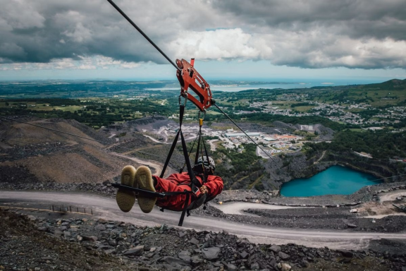 A person zip-lining over a landscape with hills and a blue lake below.