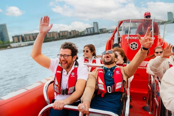 A group of people enjoying a ride on a red speedboat, smiling and waving.