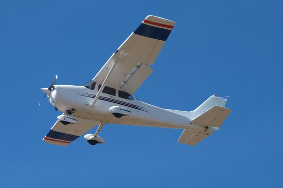 A small white aircraft flying in a clear blue sky.