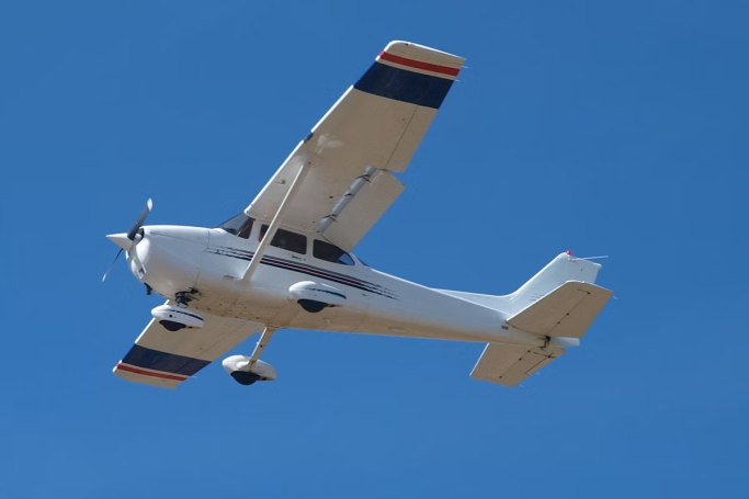 Small white aircraft flying against a clear blue sky.