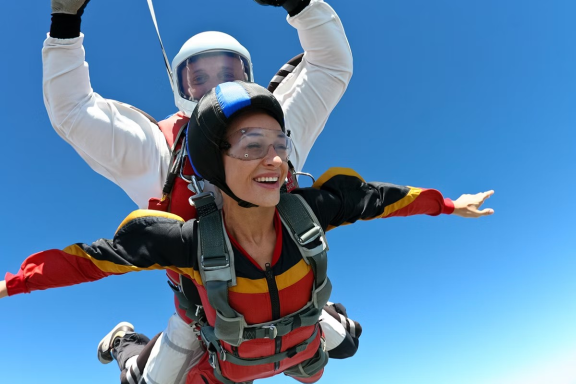 A person enjoys tandem skydiving, arms outstretched against a blue sky.